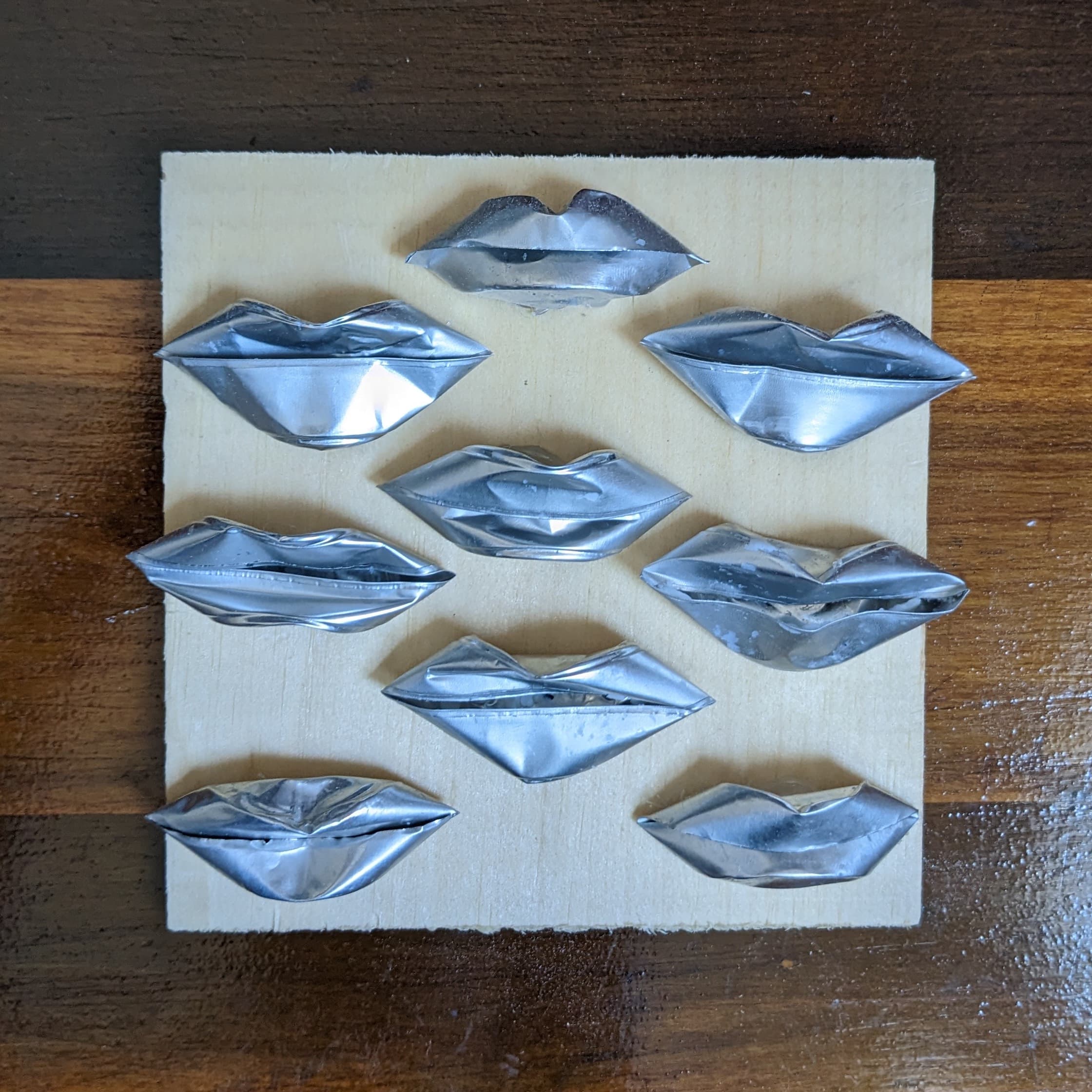 Repurposed tea light candle holders shaped like lips, adhered to a wooden base.